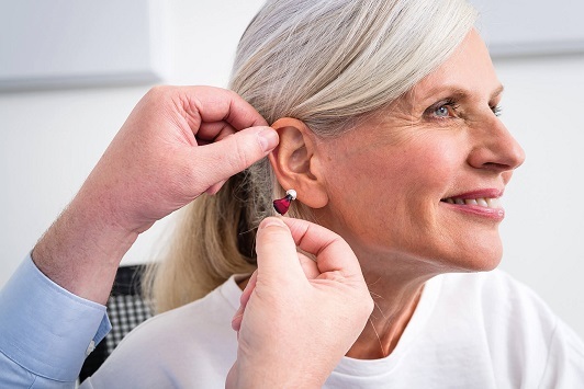 Ältere Frau bekommt ein modernes Hörgerät ins Ohr eingesetzt, Hörakustiker berät.